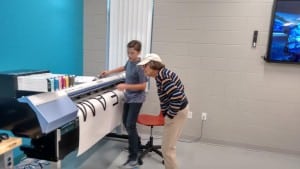 Student Winston Breeden displays a large format printer to a resident who attended the Innovation Center Open House on Oct. 7.